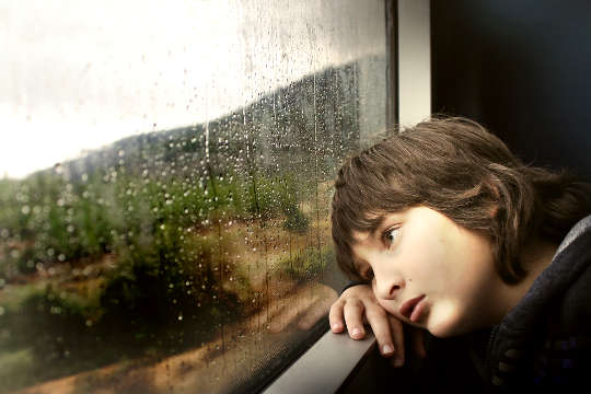 young boy looking pensively out of a window